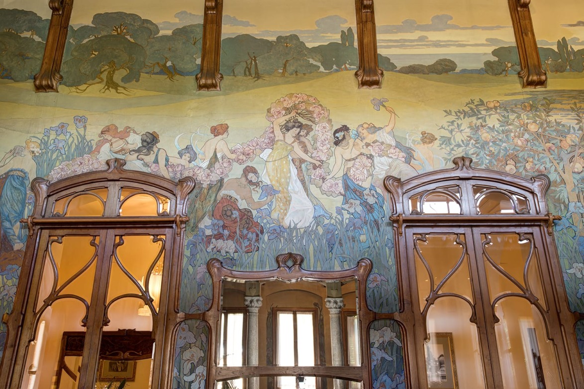 Colorful Art Nouveau mural with floral and figurative designs above ornate wooden door frames in a vintage interior setting.