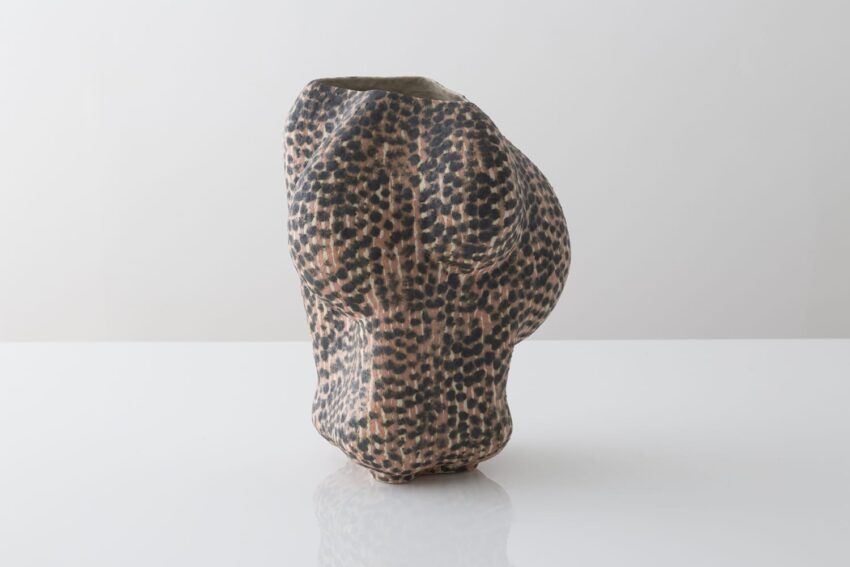 Abstract ceramic sculpture with textured, leopard-print pattern, set against a minimal white background.
