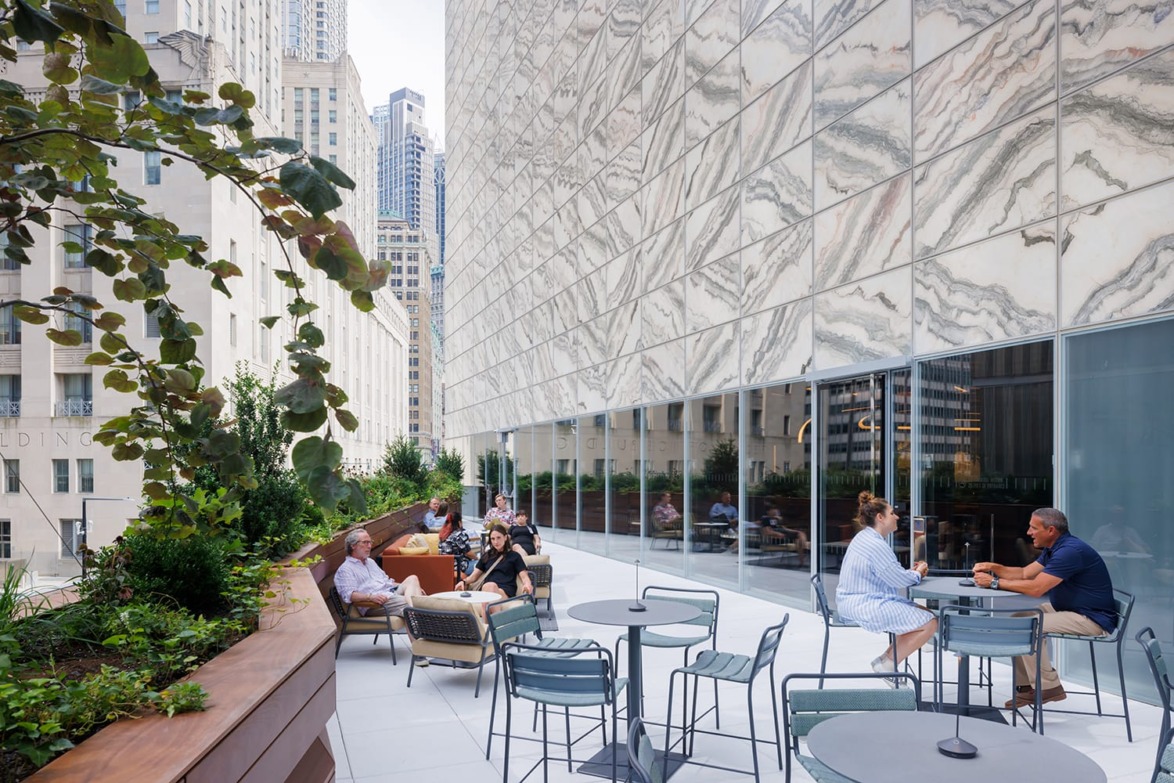 People relaxing and conversing on a modern outdoor rooftop terrace surrounded by city buildings.