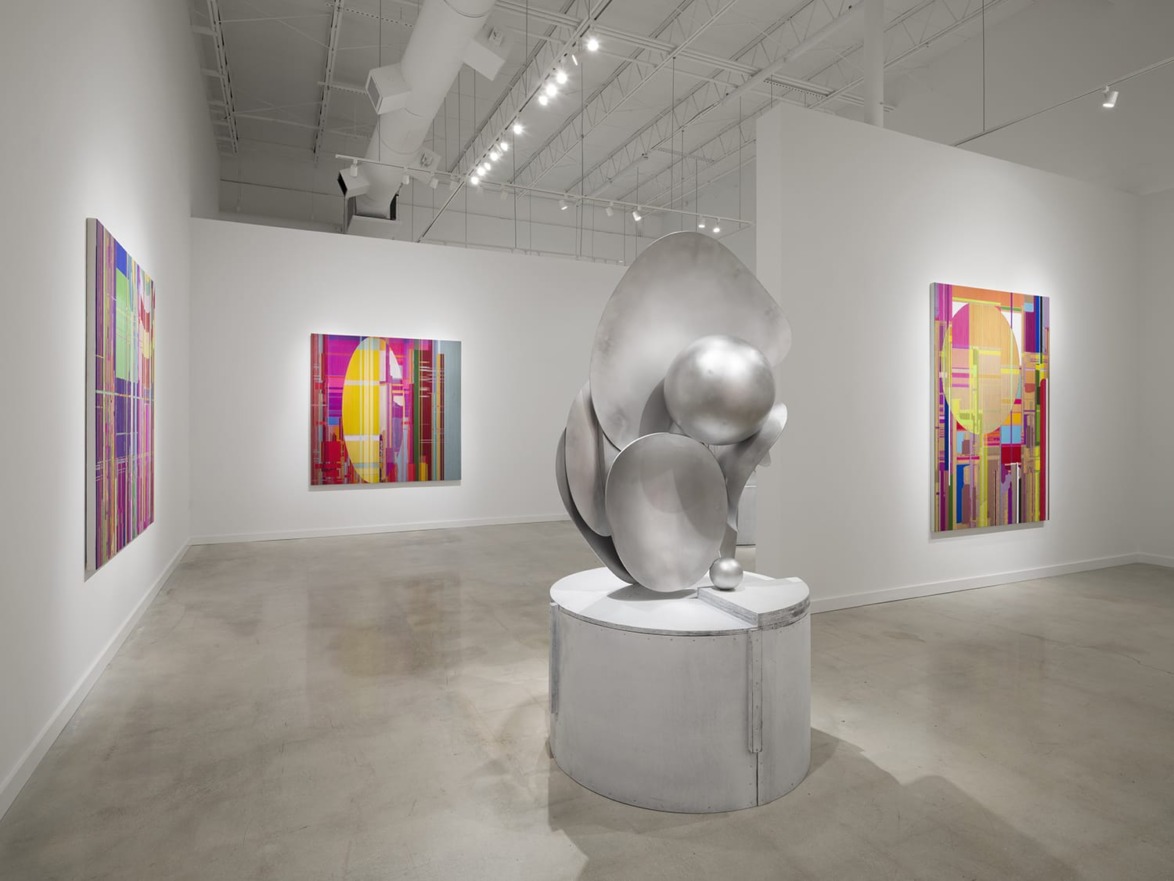 Art gallery with abstract paintings on walls and a large metallic sculpture in the center of the room.