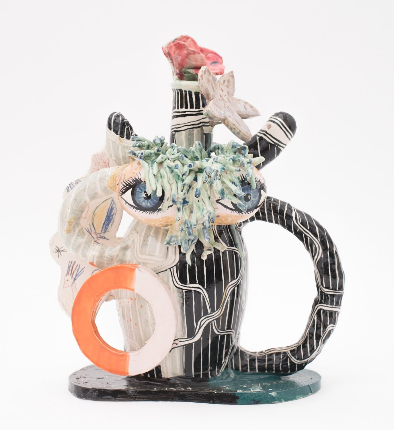 Colorful abstract ceramic sculpture with eyes, floral elements, and geometric patterns on a white background