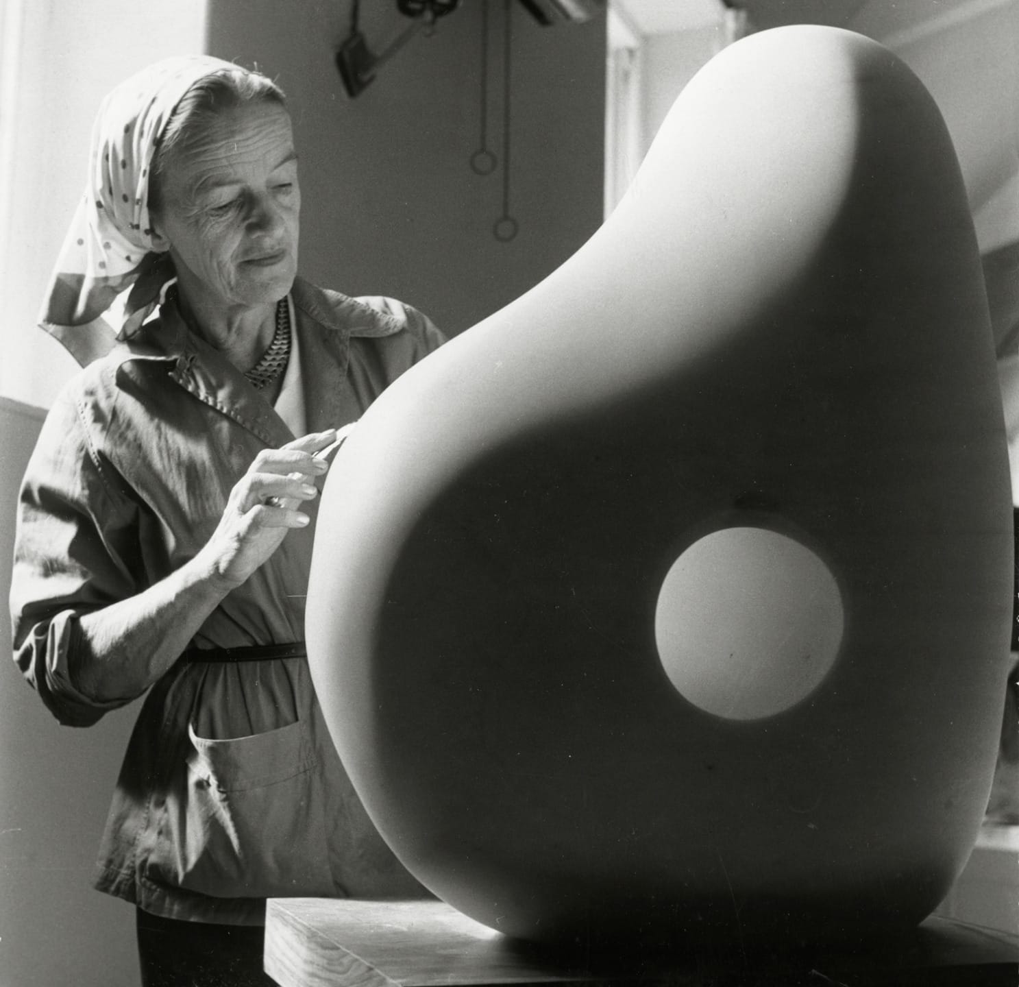 Artist working on a large, smooth abstract sculpture with a circular hole in the center in a studio setting.
