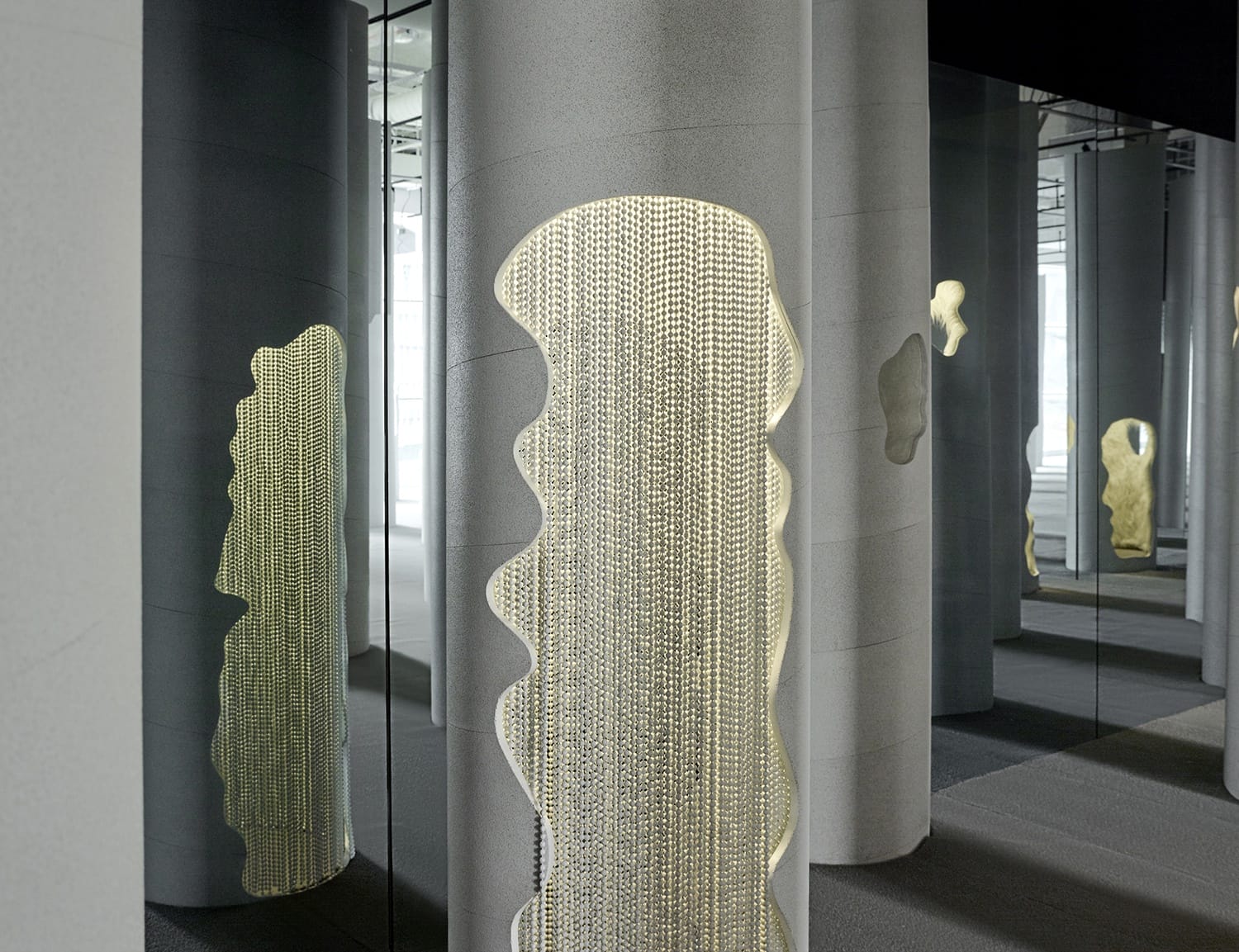 Modern art installation with vertical mirrored columns and chains creating dynamic reflections in a contemporary gallery setting