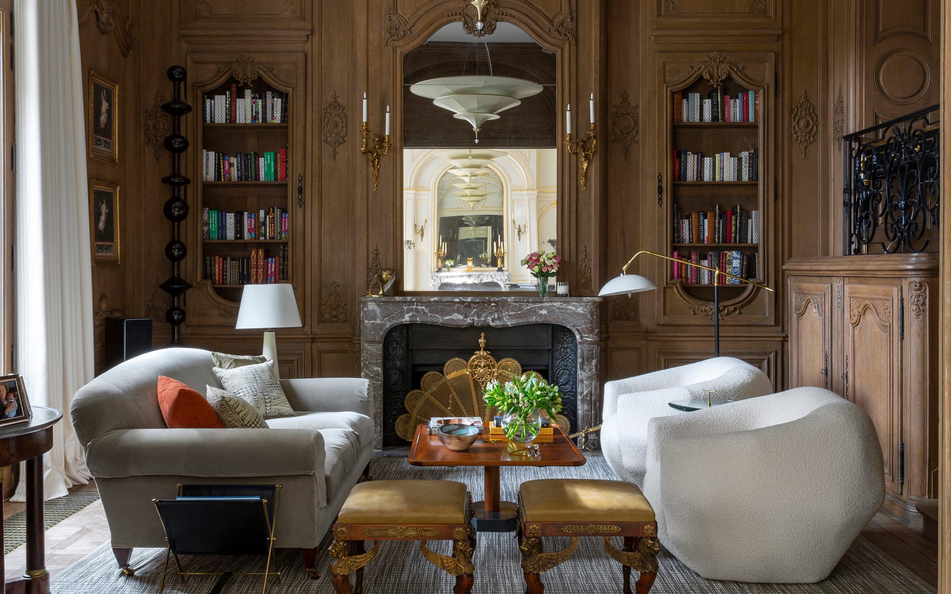 Luxurious living room with elegant furniture, ornate fireplace, large mirror, built-in bookshelves, and decorative wall paneling.