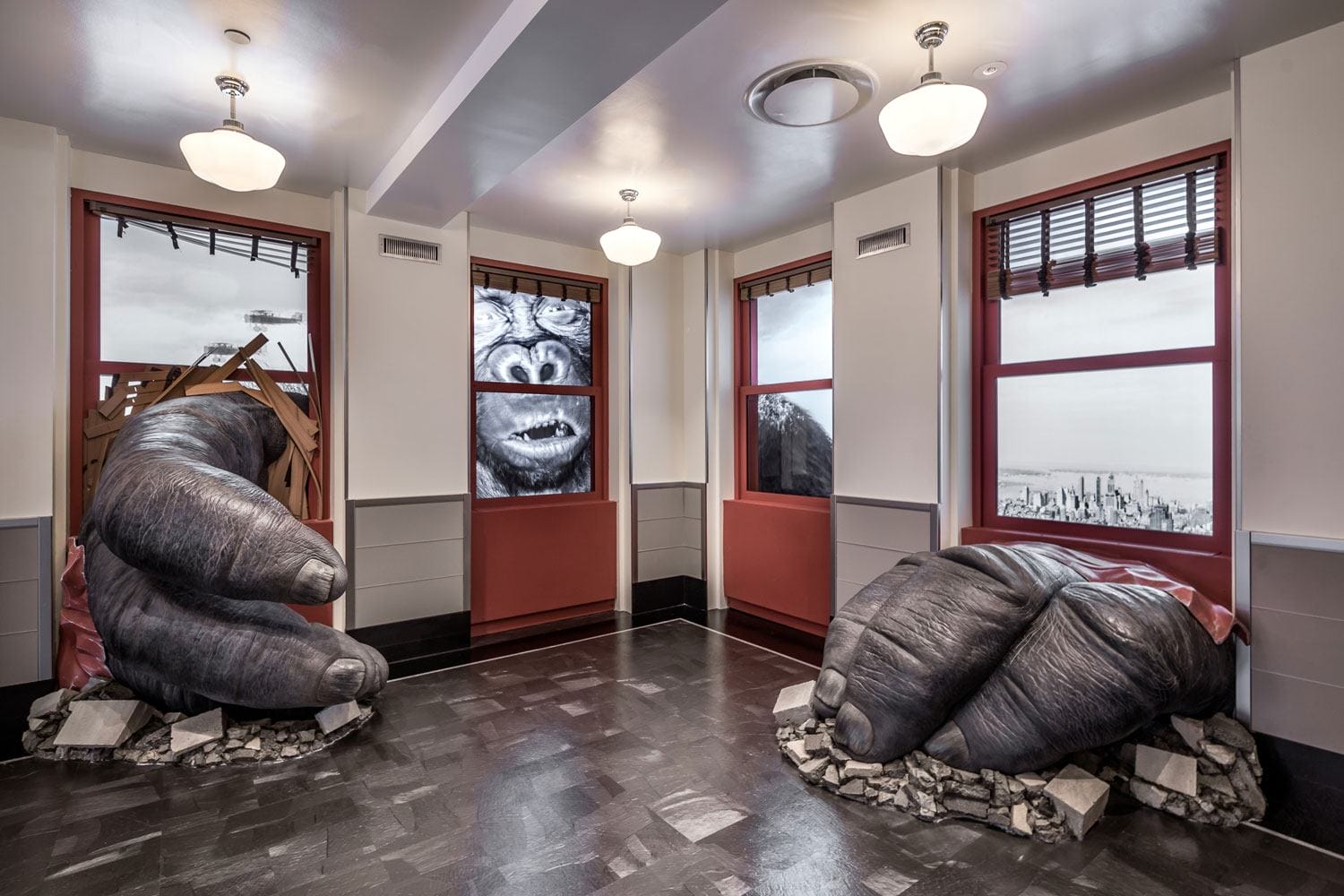 Giant gorilla hands breaking through floors and windows in a building room with cityscape view outside.