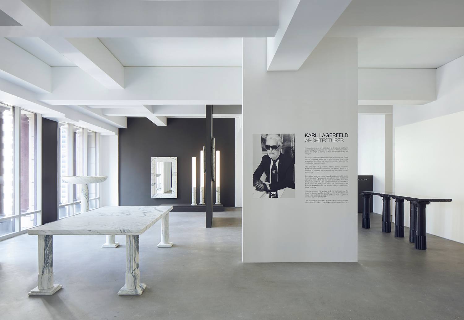 Interior view of a modern art gallery featuring minimalistic marble tables and large windows with natural light.