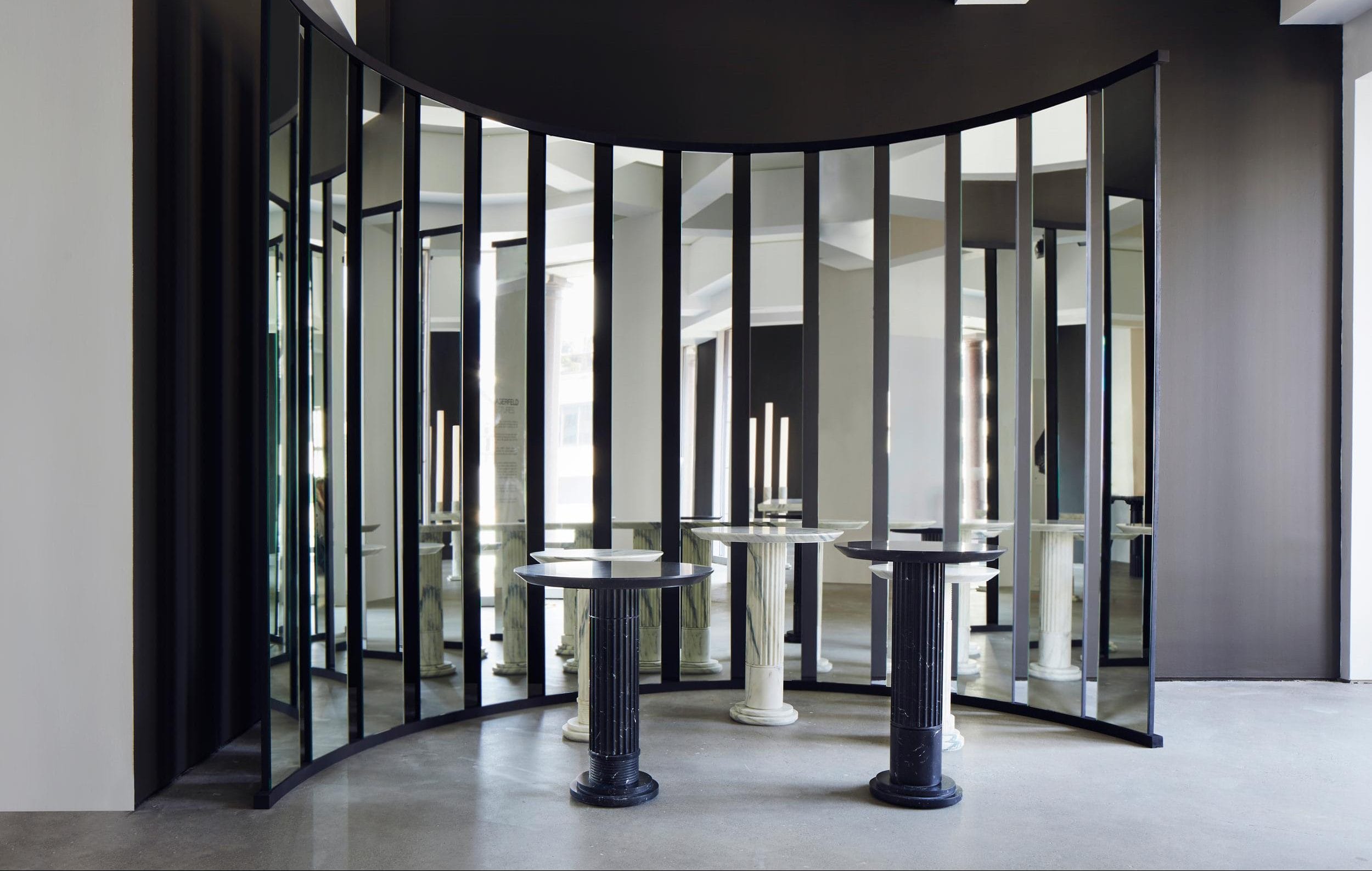 Curved black room divider with mirrors, two black pedestal tables, and a round table with candles in a modern interior.