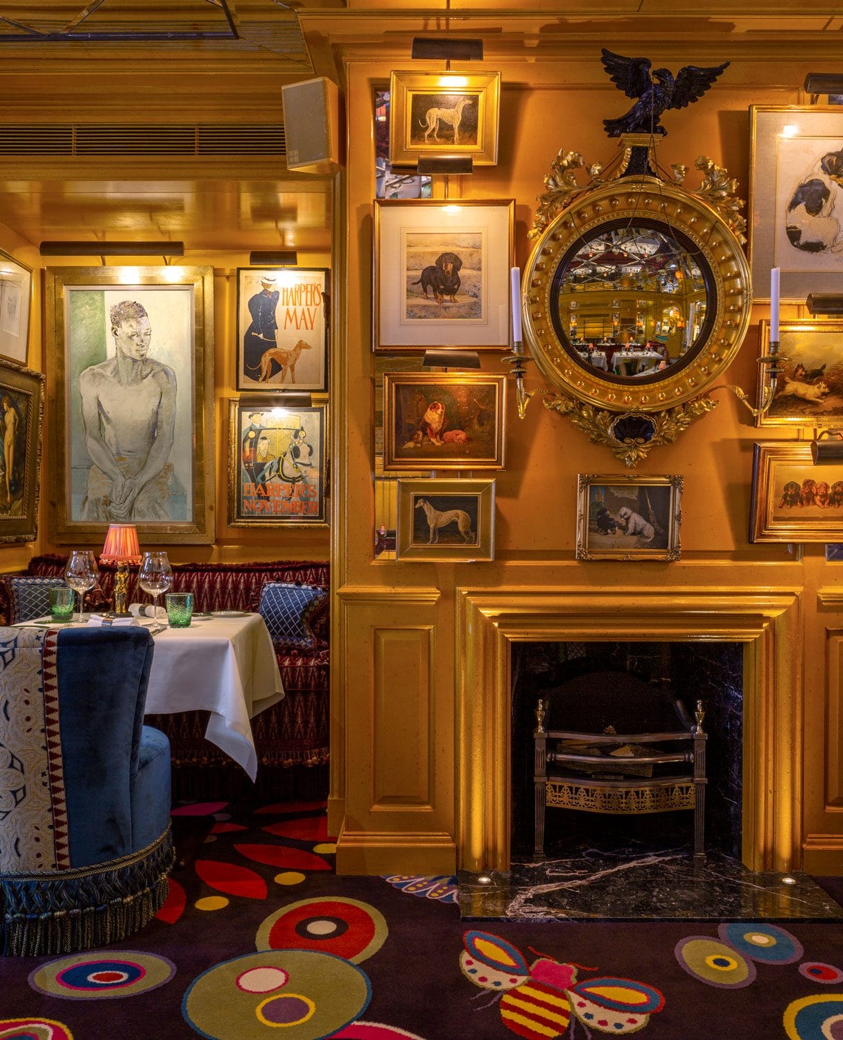 Eclectic restaurant interior with ornate mirror, framed art on mustard walls, and a set dining table by blue chairs.