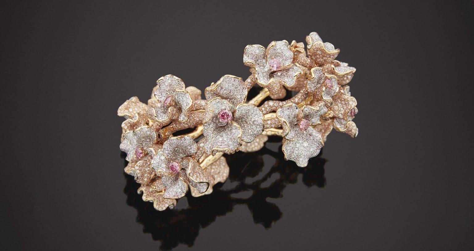Gold floral bracelet encrusted with diamonds and pink gemstones on a dark background.