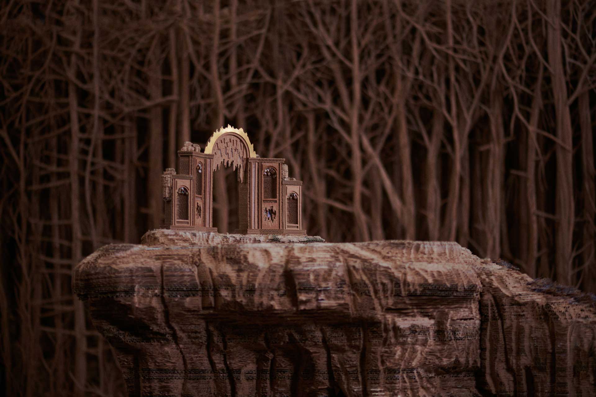 Miniature castle structure on a rocky cliff, surrounded by detailed dark, barren trees in a mysterious forest setting.
