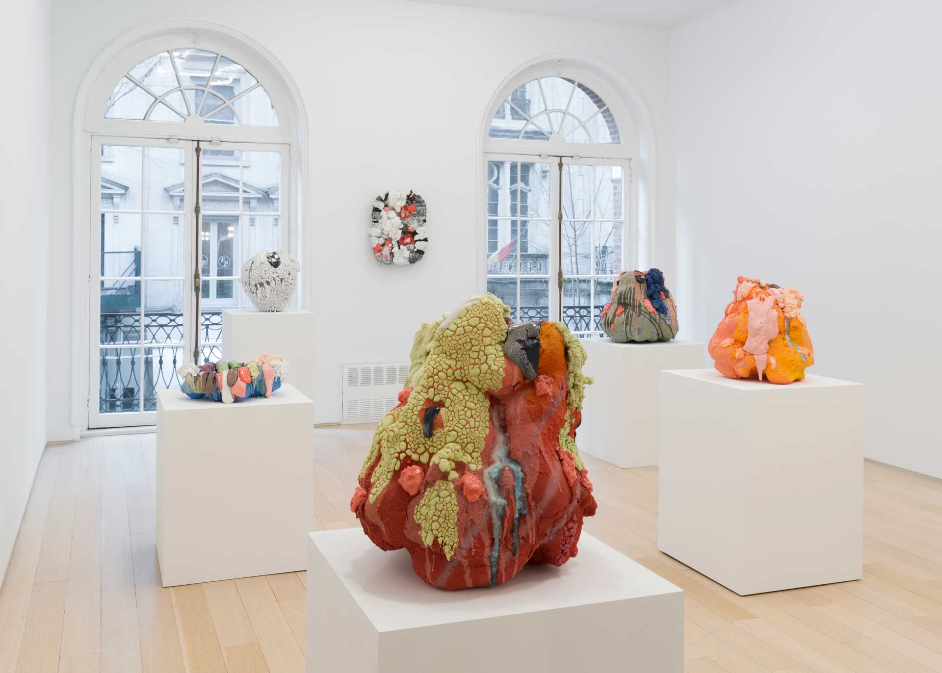 Modern art sculptures on white pedestals in a gallery with large windows and wooden floors.