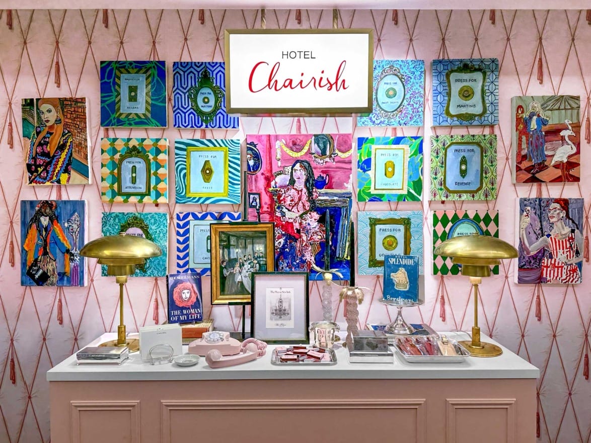 Art deco-inspired hotel display with vibrant paintings and decorative items on a table below a "Hotel Chairish" sign.