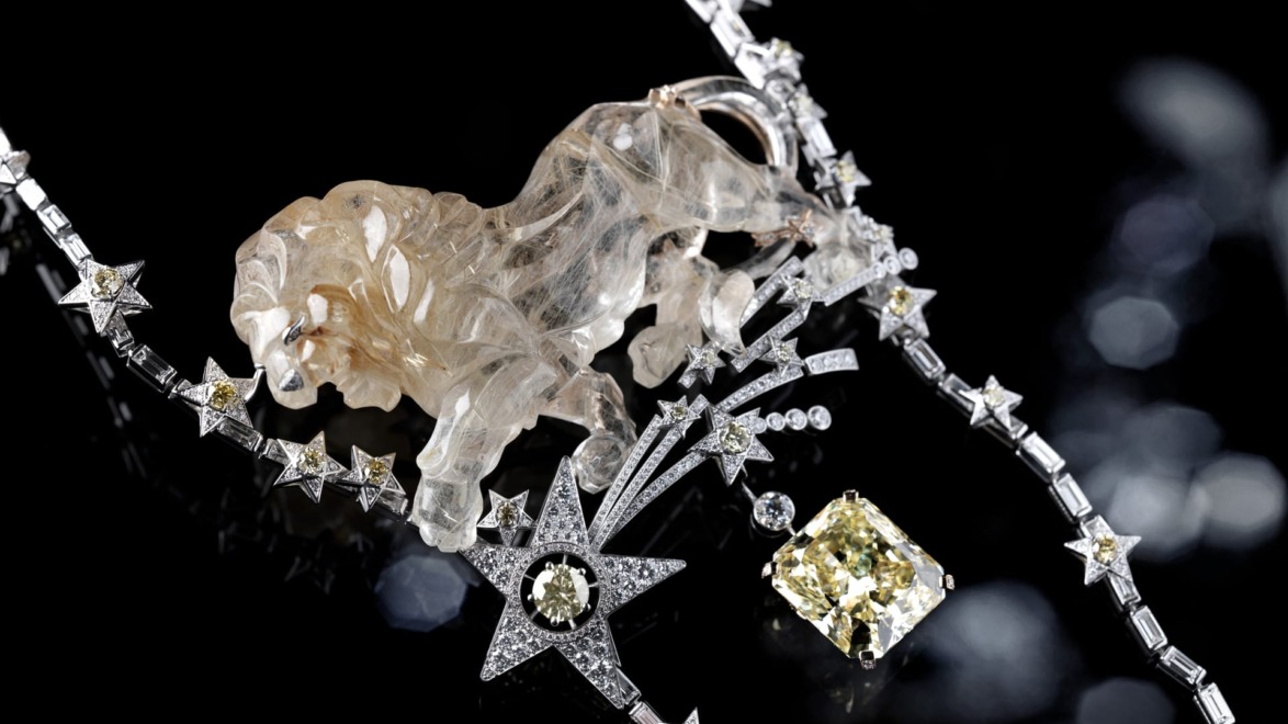 Jewelry piece with diamond stars and a carved crystal lion on a black background.