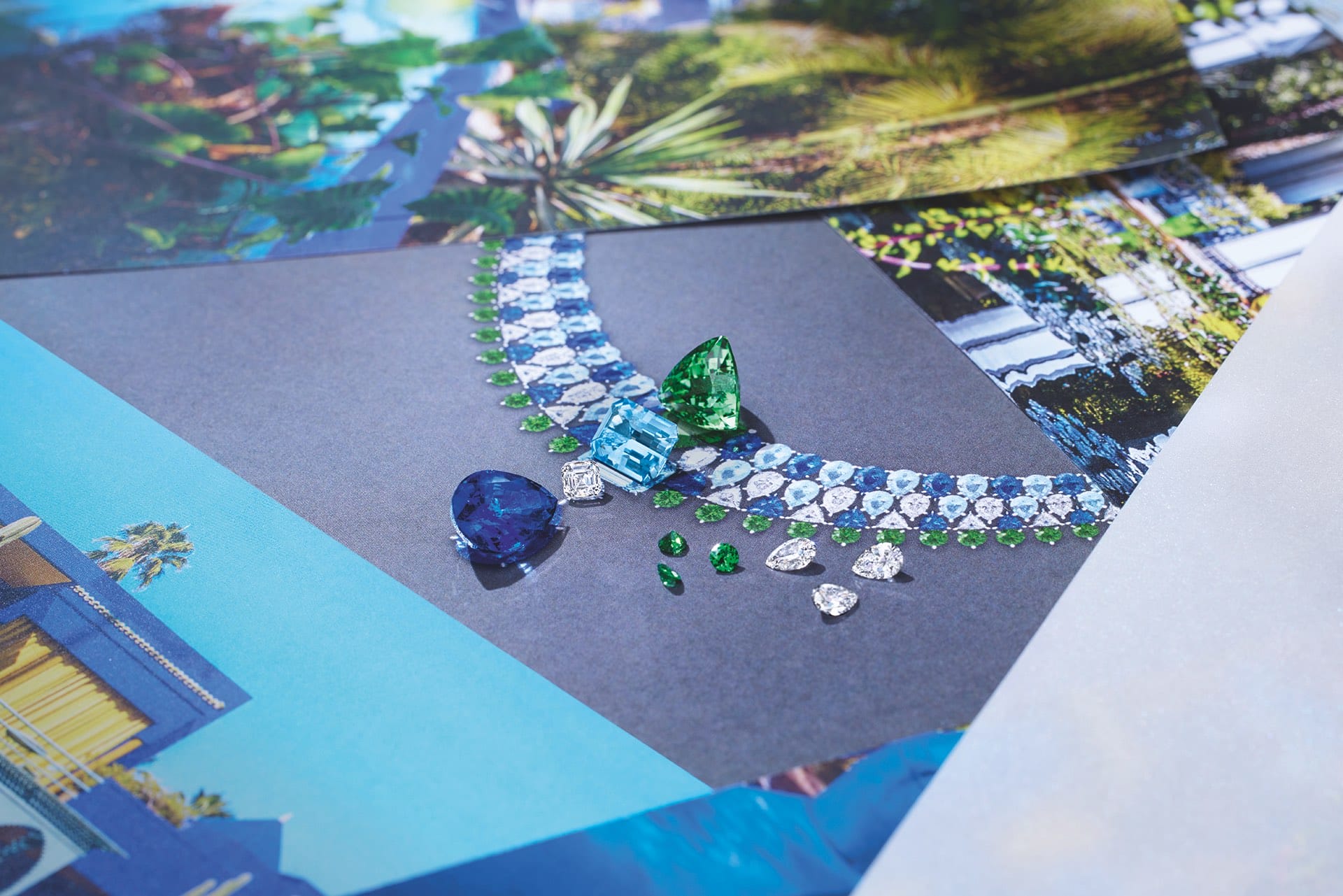 Colorful gemstone necklace with surrounding vibrant green and blue loose gems on a background of tropical images.