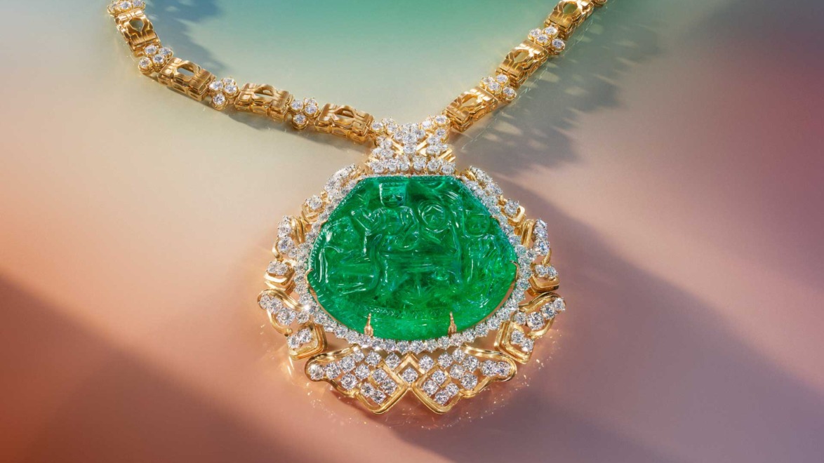 Gold and diamond necklace with large green gemstone pendant on a colorful gradient background.