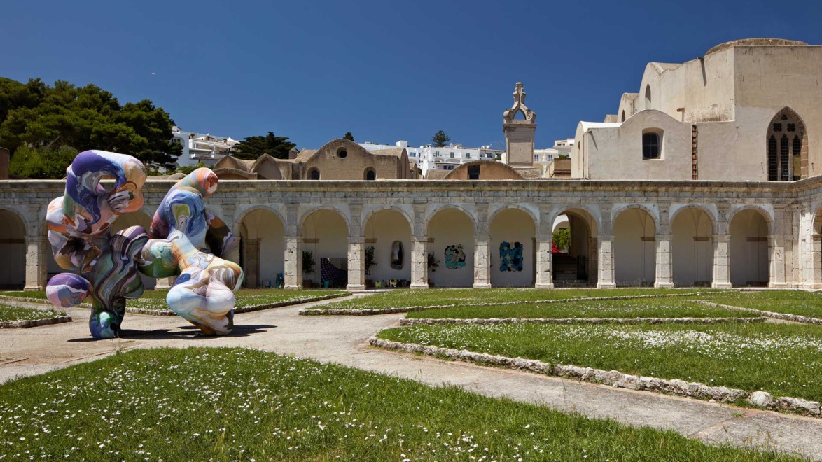 Outdoor sculpture and historic architecture under a clear blue sky, surrounded by grass and pathways.