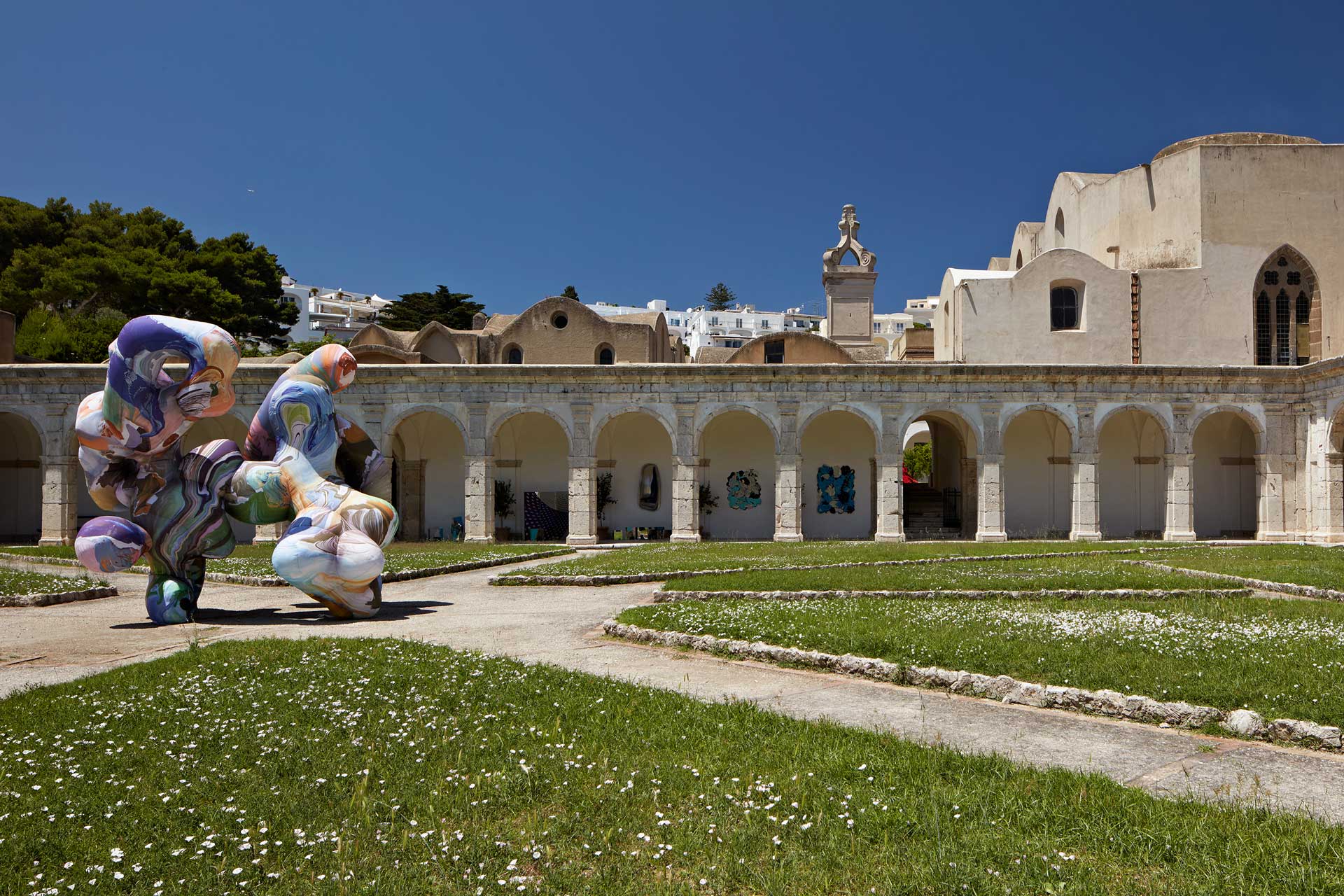 Outdoor sculpture and historic architecture under a clear blue sky, surrounded by grass and pathways.