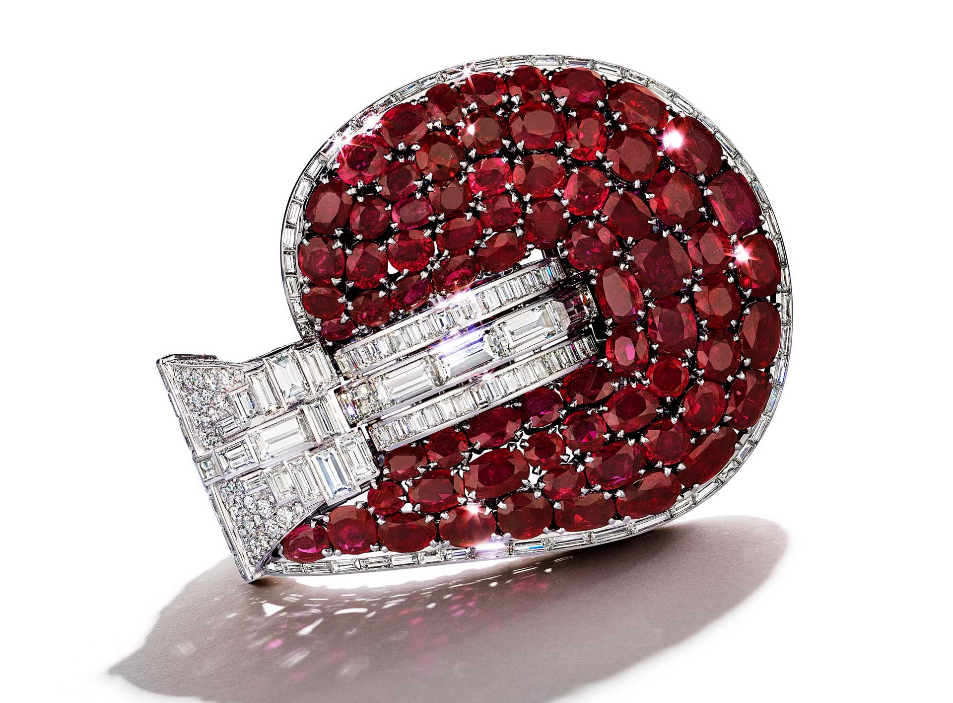 Luxurious brooch adorned with numerous red gemstones and diamonds on a white background, casting a slight shadow.
