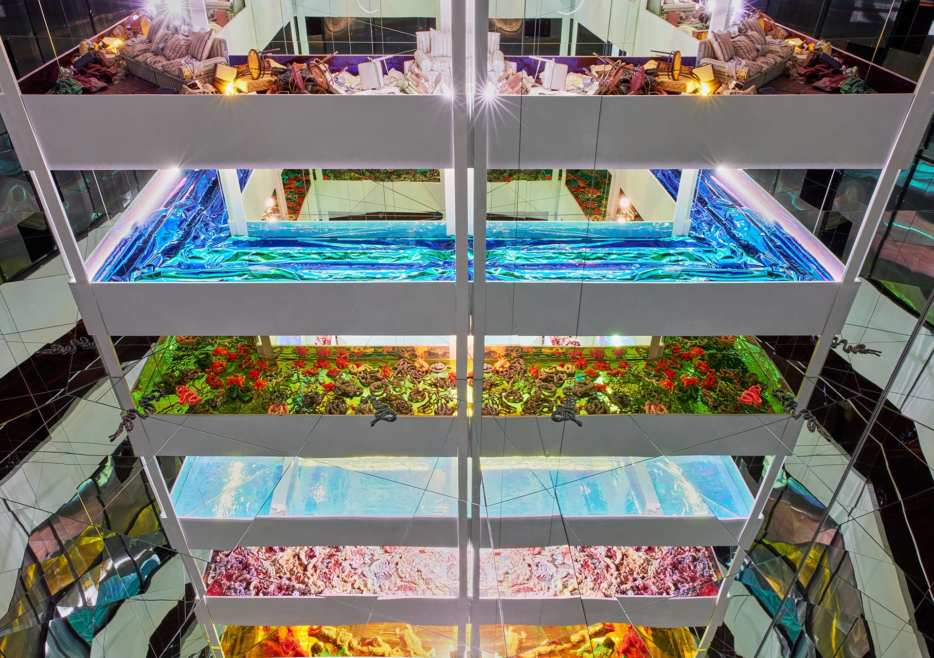 Luxurious indoor atrium with vibrant multicolored lights, water pool, and greenery across multiple levels in a modern hotel.