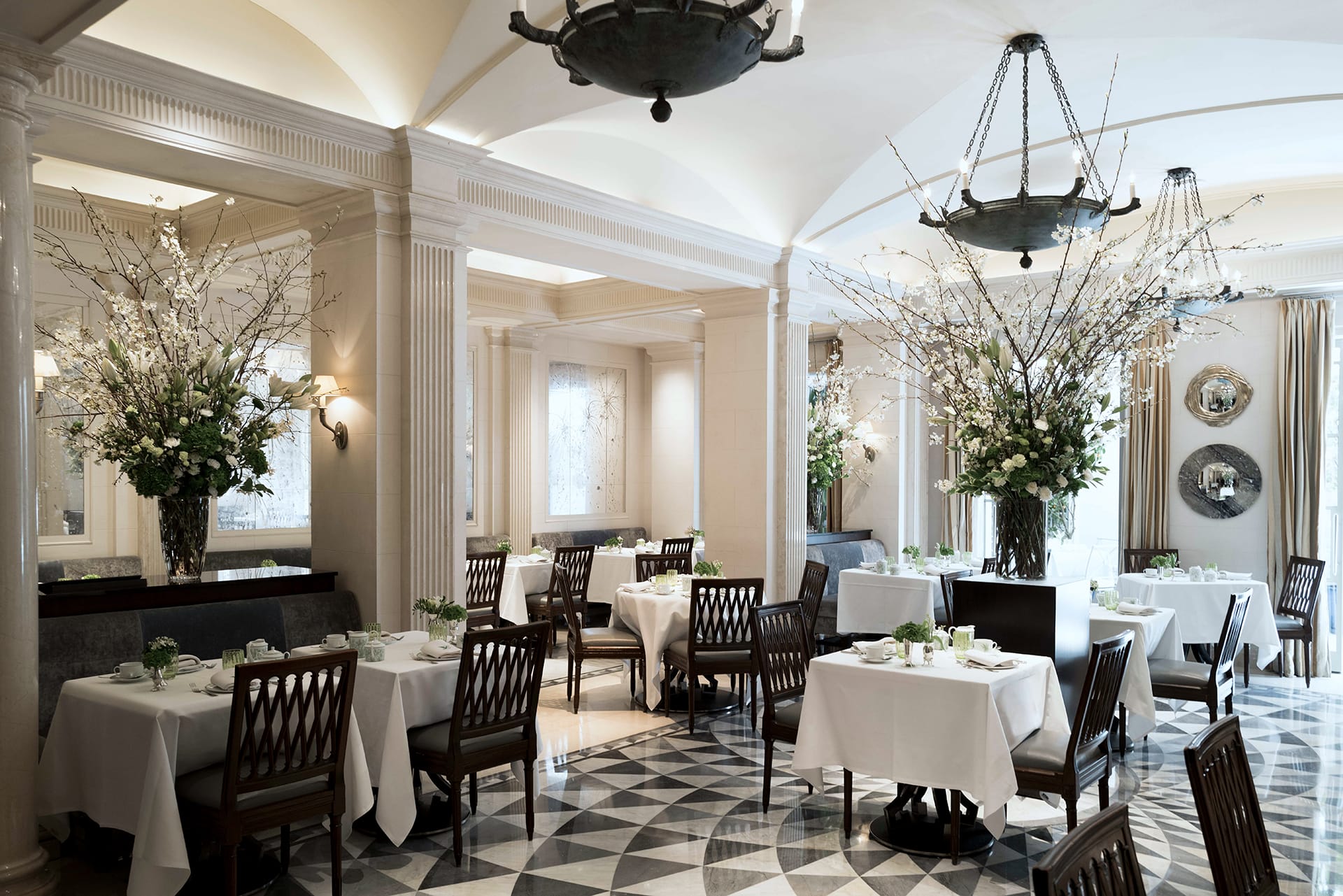 Elegant restaurant interior with white tablecloths, floral arrangements, and decorative chandeliers.