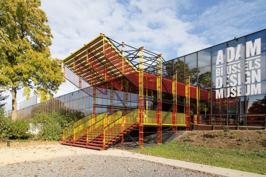 Colorful outdoor staircase at ADAM Brussels Design Museum against a glass facade and trees under a blue sky.