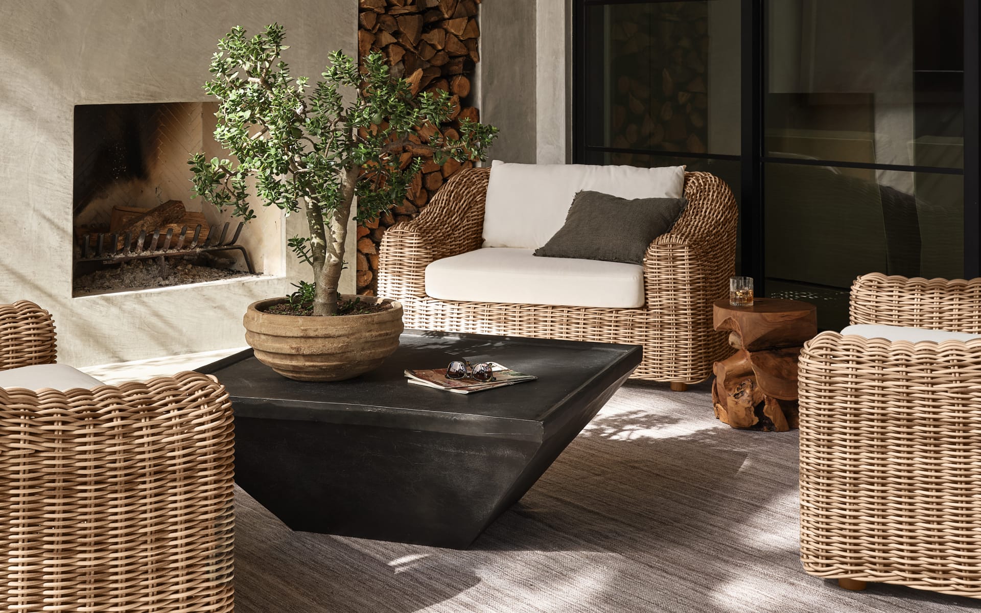 Outdoor seating area with wicker chairs, black table, fireplace, and a potted plant, creating a cozy and inviting atmosphere.
