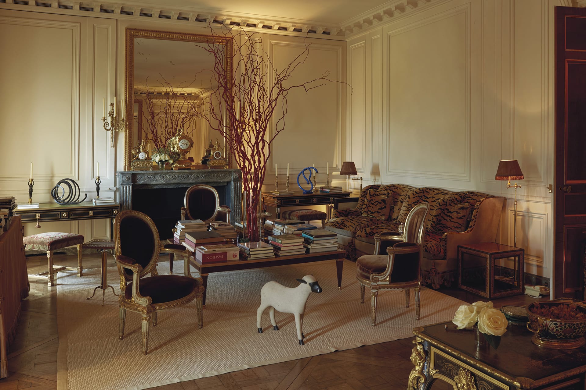 Elegant living room with classic furniture, large mirror, decorative branches on table, and cozy lighting.
