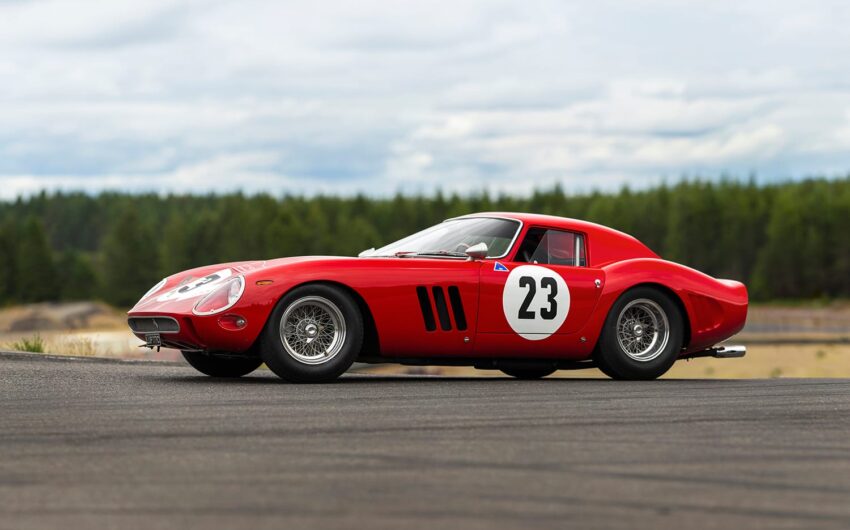Red vintage race car with number 23 on side, parked on asphalt with a forest background.