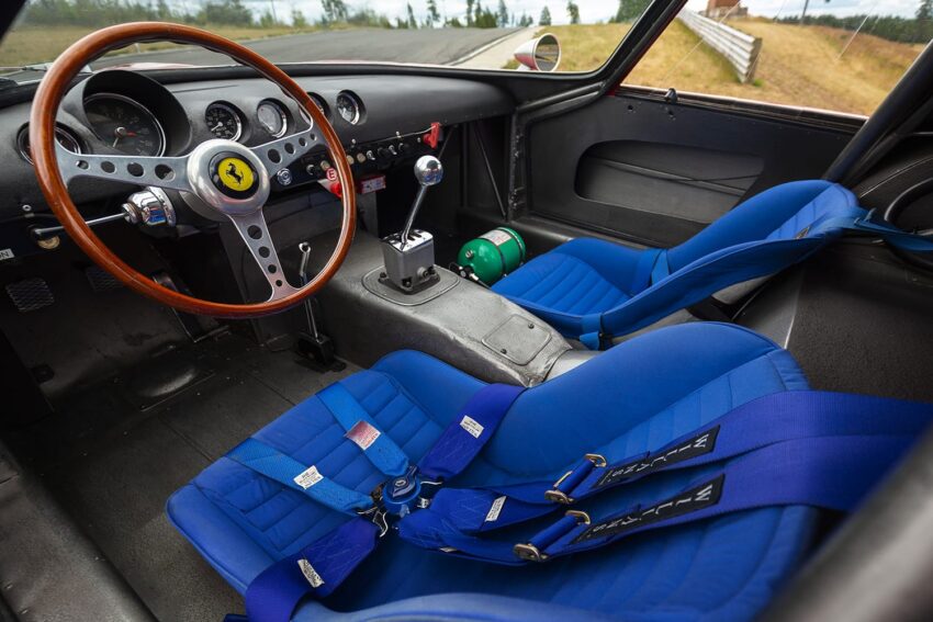 Vintage car interior with wood steering wheel, blue racing seats, and gearshift.