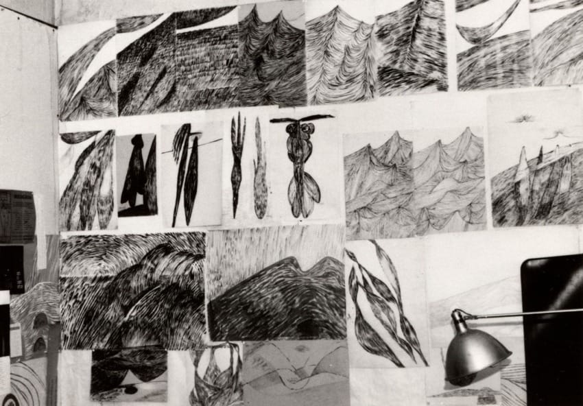 Wall with various abstract black and white sketches featuring waves, mountains, and abstract forms, lit by a desk lamp.