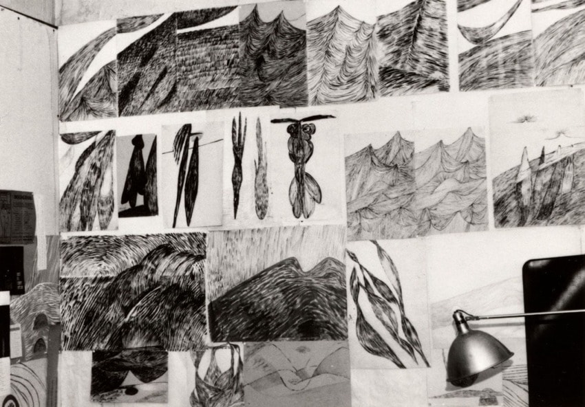 Wall with various abstract black and white sketches featuring waves, mountains, and abstract forms, lit by a desk lamp.