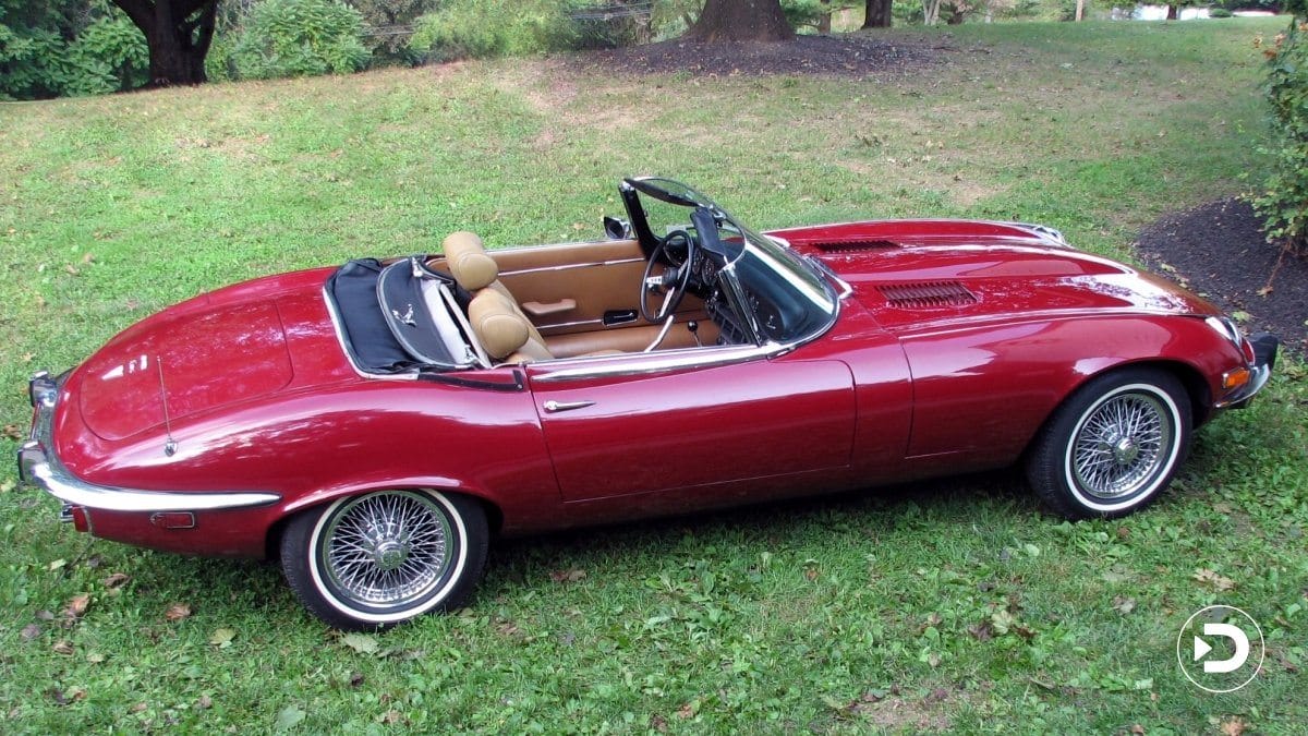 Red vintage convertible car parked on grass in a park setting.