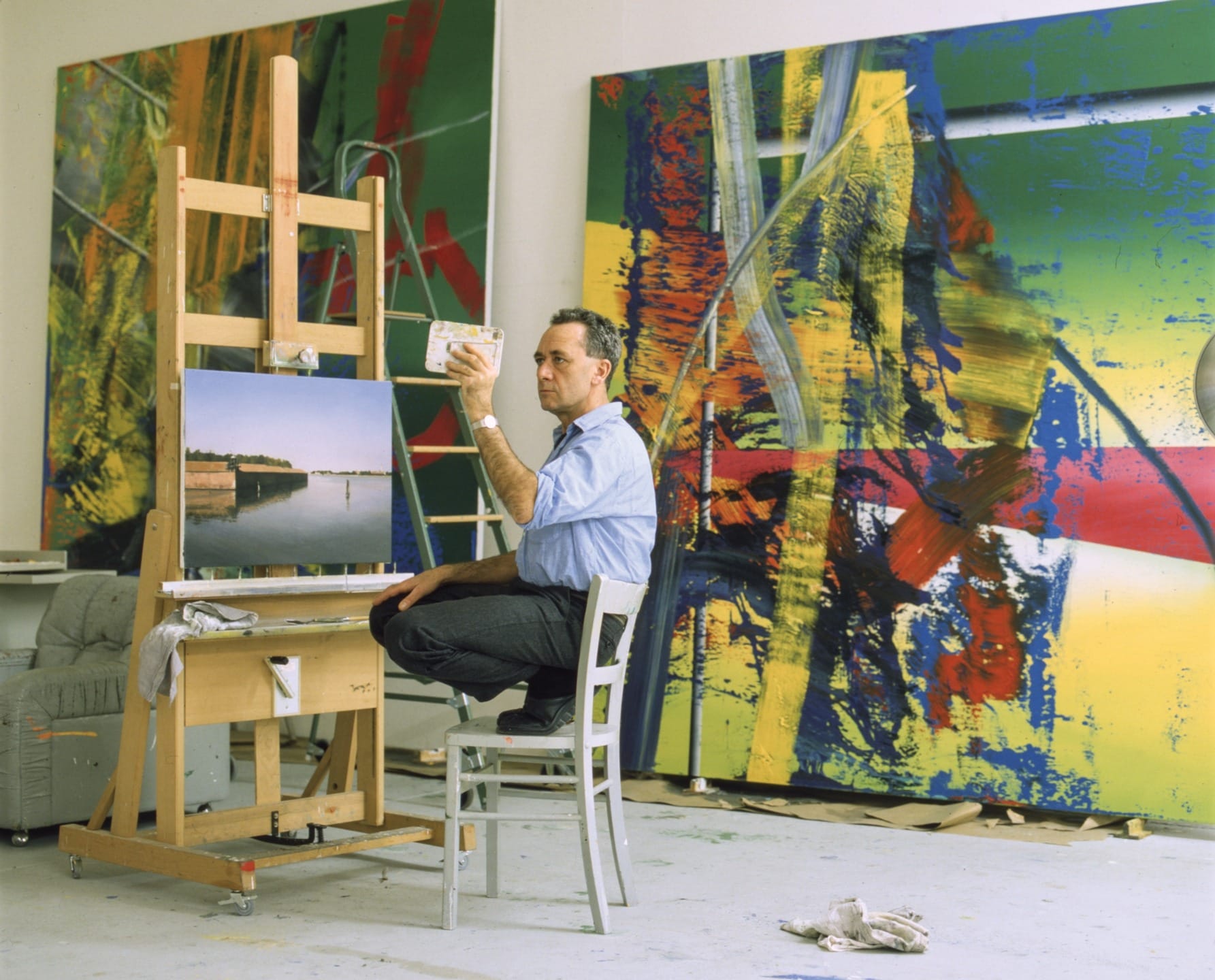 Artist painting on canvas in a studio filled with large colorful abstract artworks in the background.