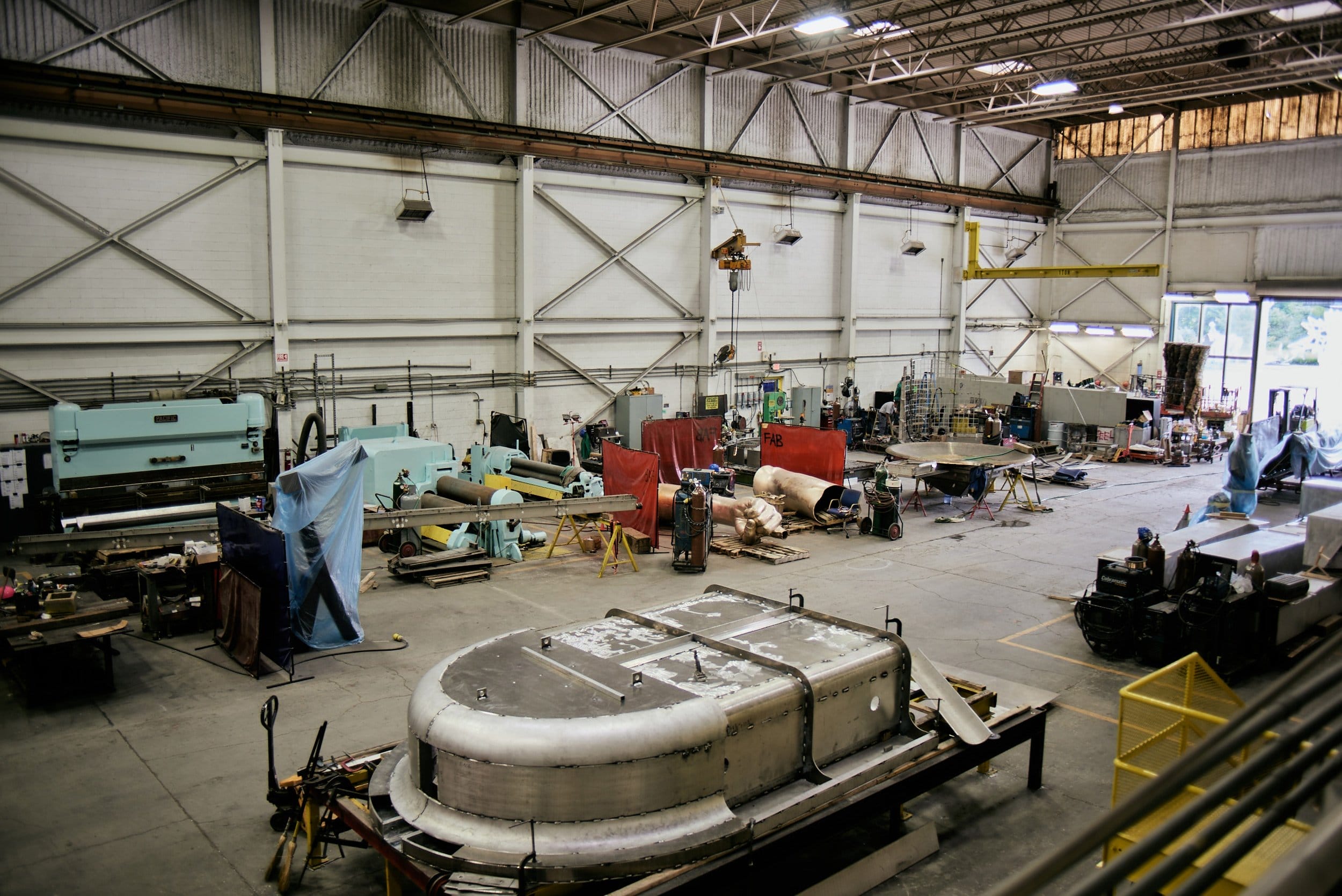 Interior view of a large industrial workshop with machinery, equipment, and various materials scattered around.