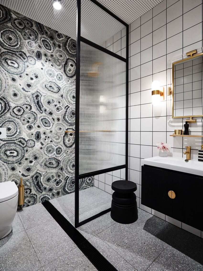 Modern bathroom with black and white tiles, glass shower partition, black stool, and decorative wall tiles.