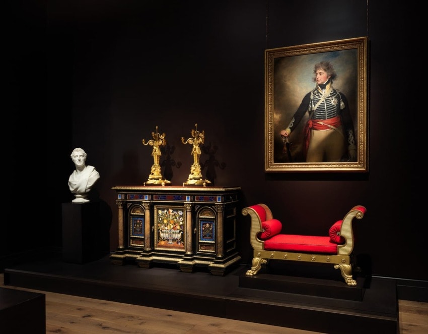 Elegant museum display with a portrait of a soldier, ornate furniture, two candlesticks, and a white bust on a pedestal.