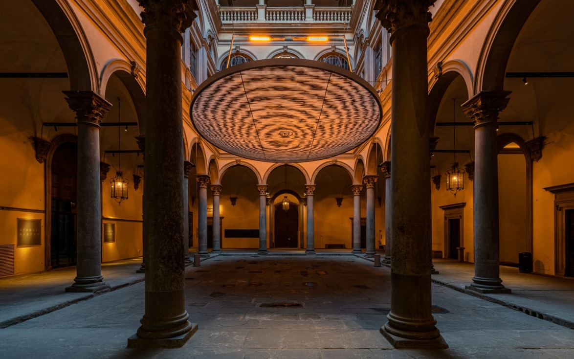 Interior courtyard with stone columns and an artistic circular ceiling feature illuminated by soft lighting.