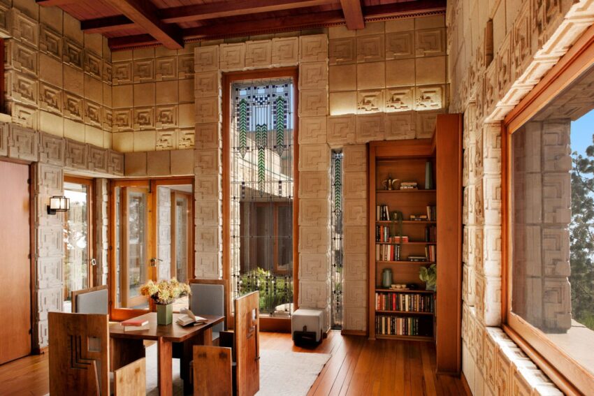 Dining room with geometric patterns, wooden furniture, bookshelves, and large windows overlooking a lush outdoor garden.