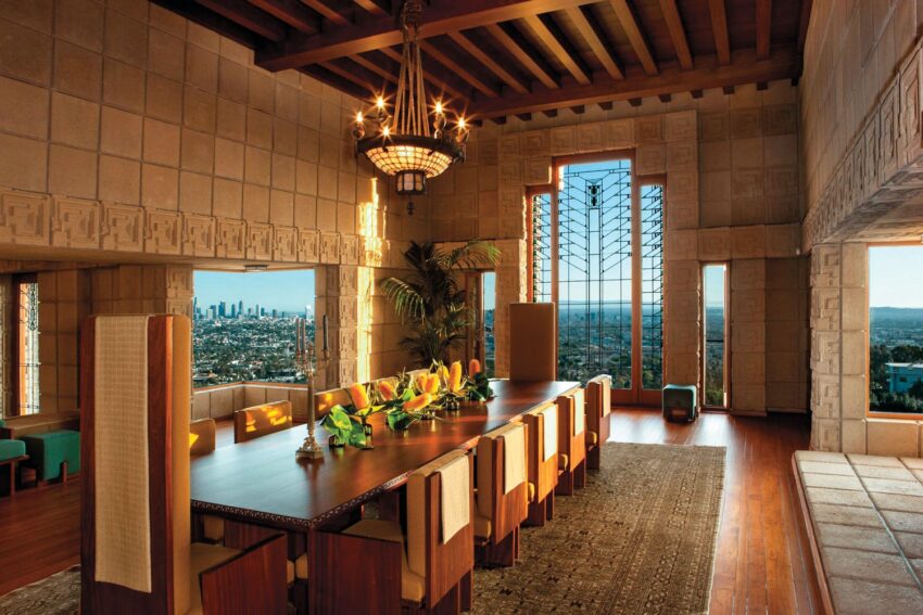 Spacious dining room with a large table, chandelier, and city skyline view through tall windows.