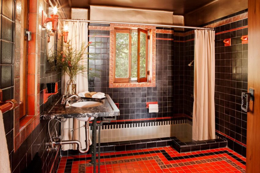 Vintage bathroom with black and red tiles, marble sink, and curtained bathtub next to a window.