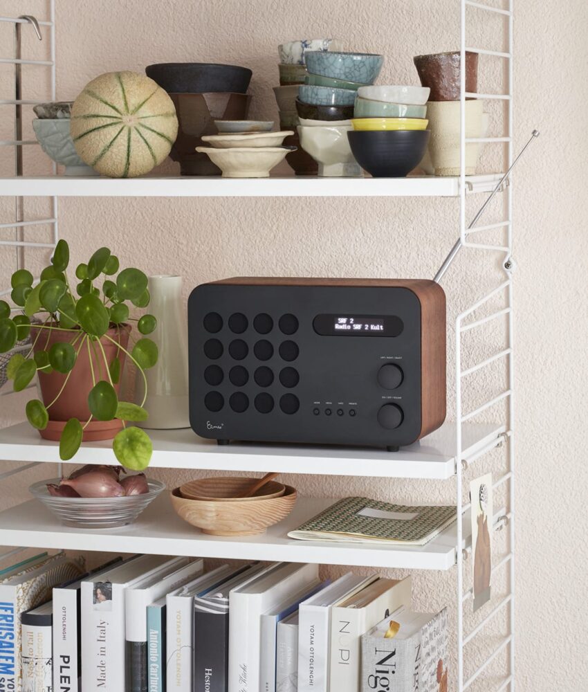 Vintage-style radio on a white shelf decorated with various ceramic bowls and a small potted plant, against a peach wall.