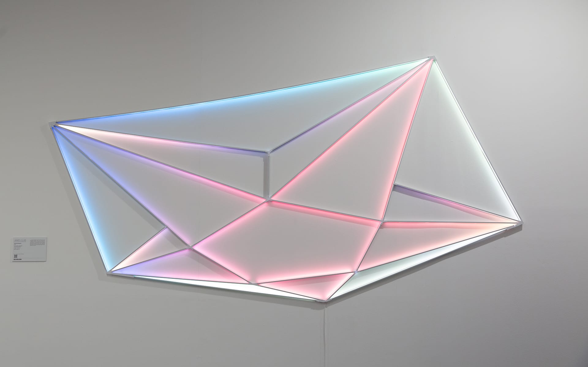 Geometric wall art installation with glowing neon lights in pink and blue shades on a gray background.