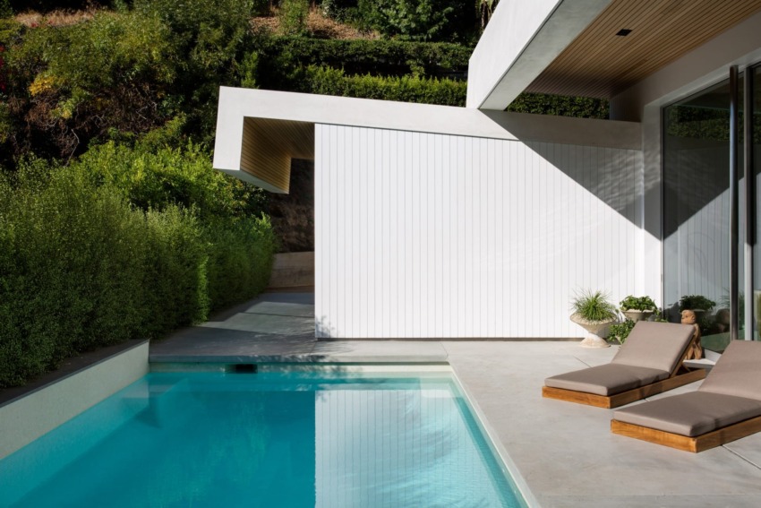 Modern house with a sleek design, poolside view, two lounge chairs, and lush greenery.