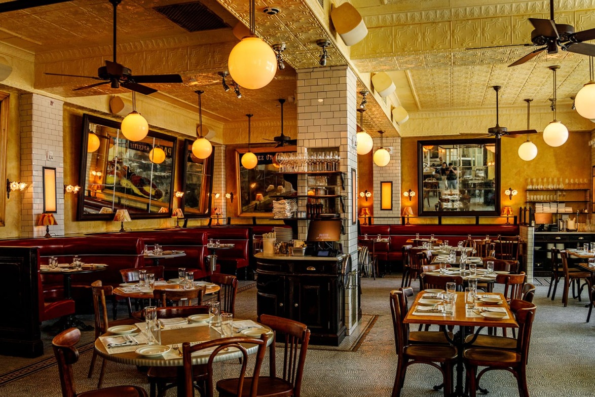 Cozy vintage restaurant interior with wooden chairs, tables set, warm lighting, and decorative mirrors on the walls.