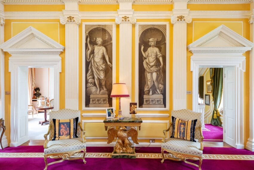 Elegant living room with classical statues, ornate furniture, yellow walls, and a purple carpet, showcasing a luxurious design.