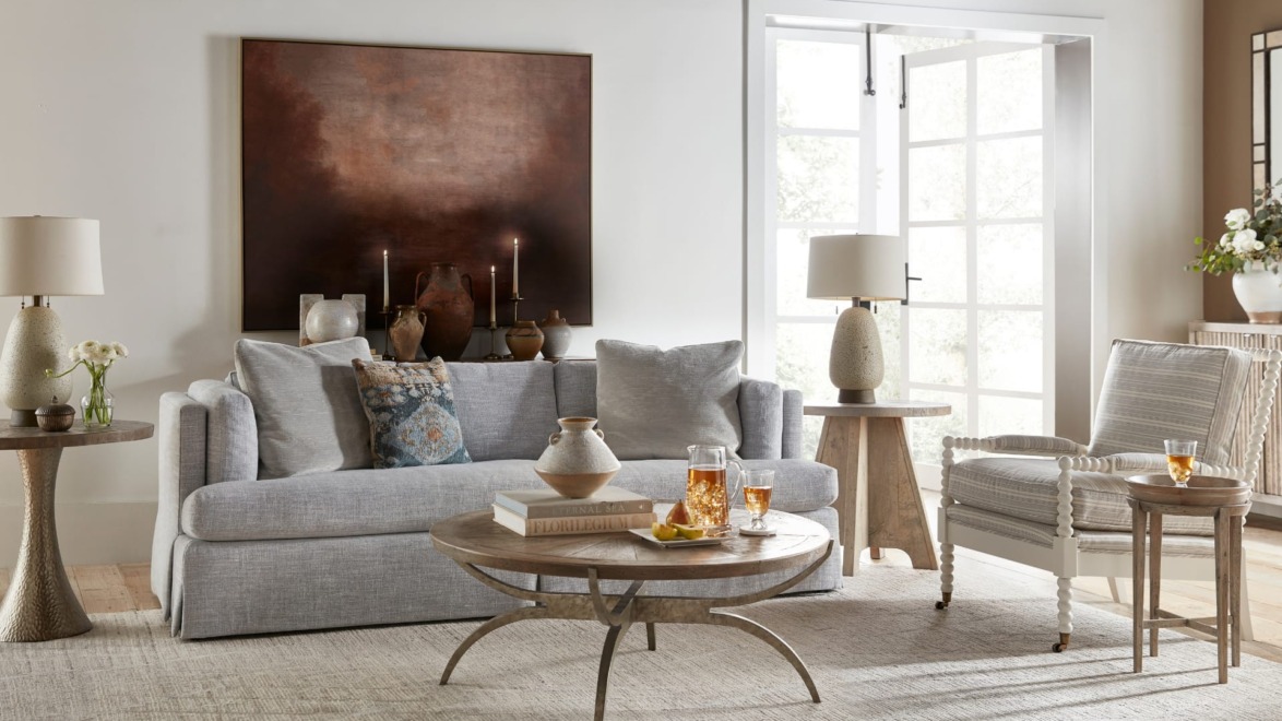 Modern living room with gray sofa, wooden coffee table, side tables, and decorative items in a bright, airy space.