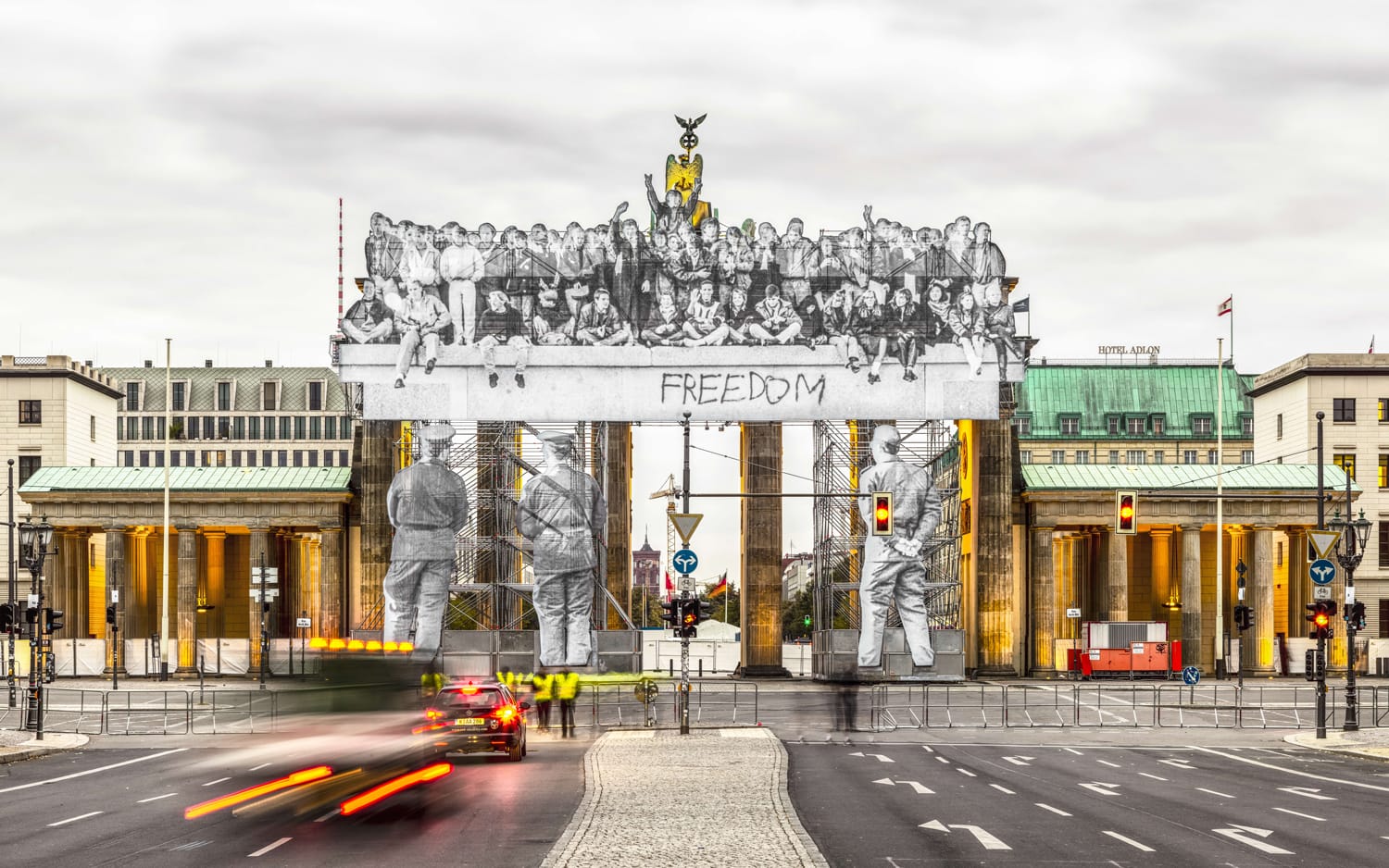 Brandenburg Gate with artistic overlay of people and "Freedom" graffiti; motion blur on nearby traffic.