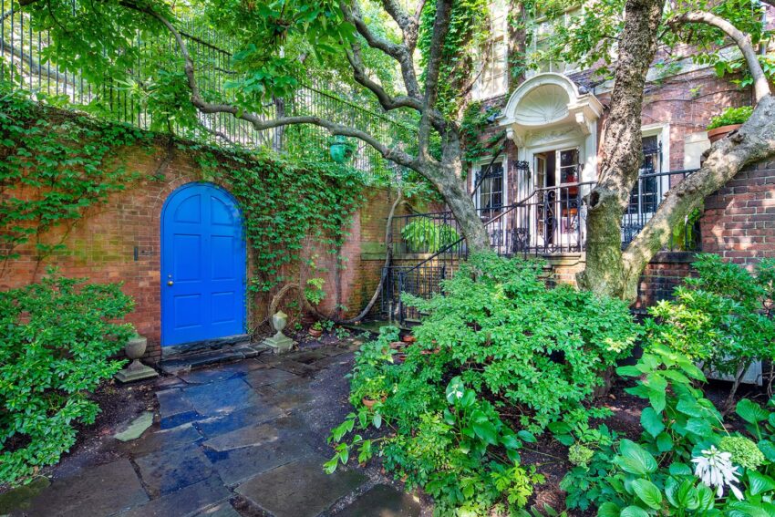 lush garden courtyard with stone path, vibrant green plants, and a striking blue door under an old brick building with ivy