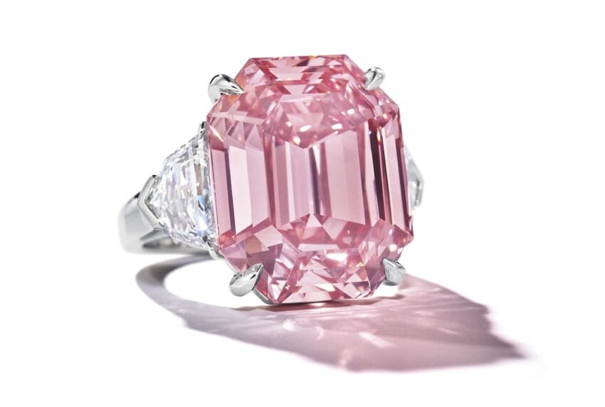 Large pink diamond ring with two clear diamonds on a reflective surface.