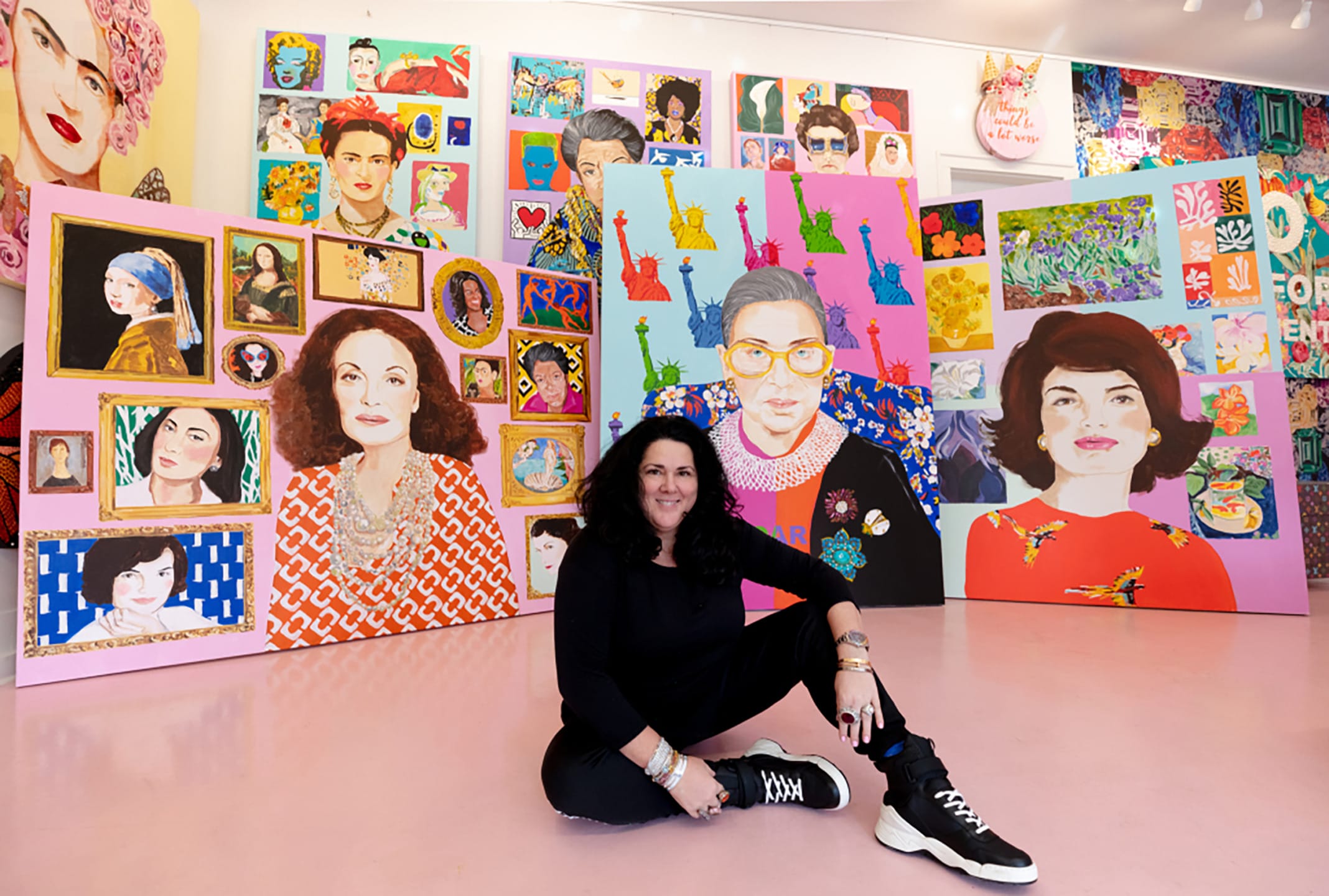 Person sitting on a pink floor surrounded by colorful pop art portraits and paintings in a gallery setting.